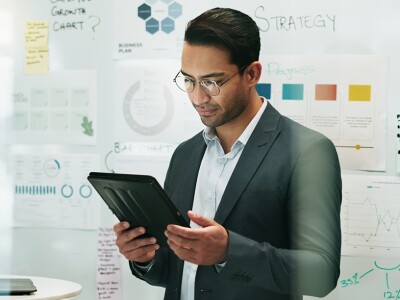 A business analyst reviews data on a tablet, surrounded by strategy charts and graphs in an office