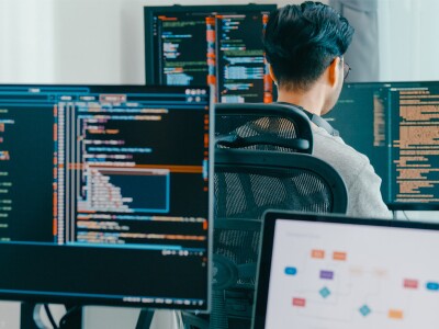 Two workers sit at desks in front of computer screens with data in the displays.