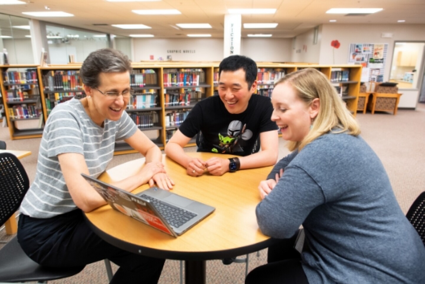 Three students in a library looking at a laptop together