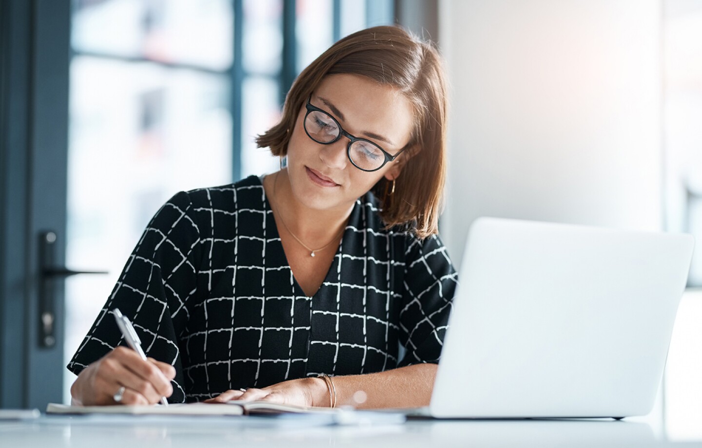 Woman working at a laptop and writing in a notebook
