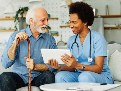 Elderly man holding cane speaking with Geriatric care nurse on couch