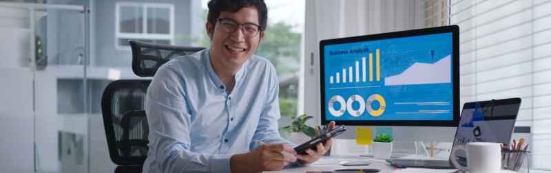 Portrait head shot of young attractive asian man reviewing finance data on computer.