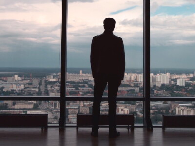 Man in suit standing in front of a window in a high-rise building.