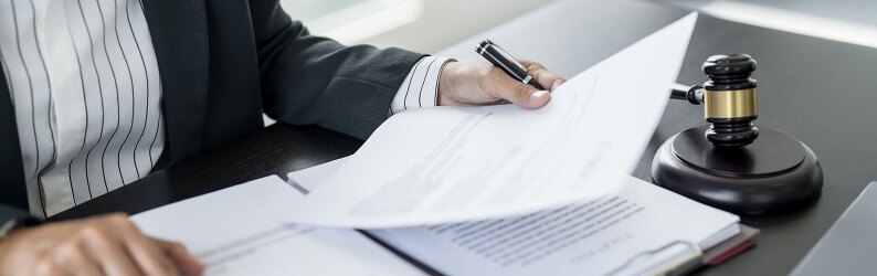 A law attorney reviewing legal documents at a desk with a legal contract and a pen.