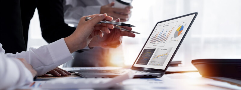 Hands of two people using pens to point at the charts on an open laptop.