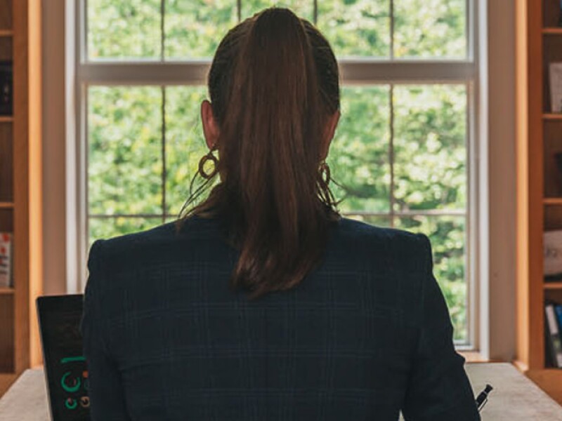 Woman sits at computer with her back to the camera. She's in front of a window in what seems to be a bookstore or a library.