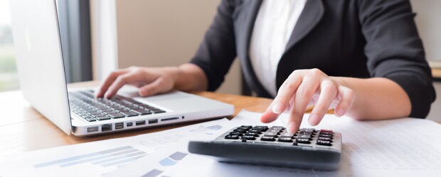 Person with a hand on laptop and a hand on a calculator