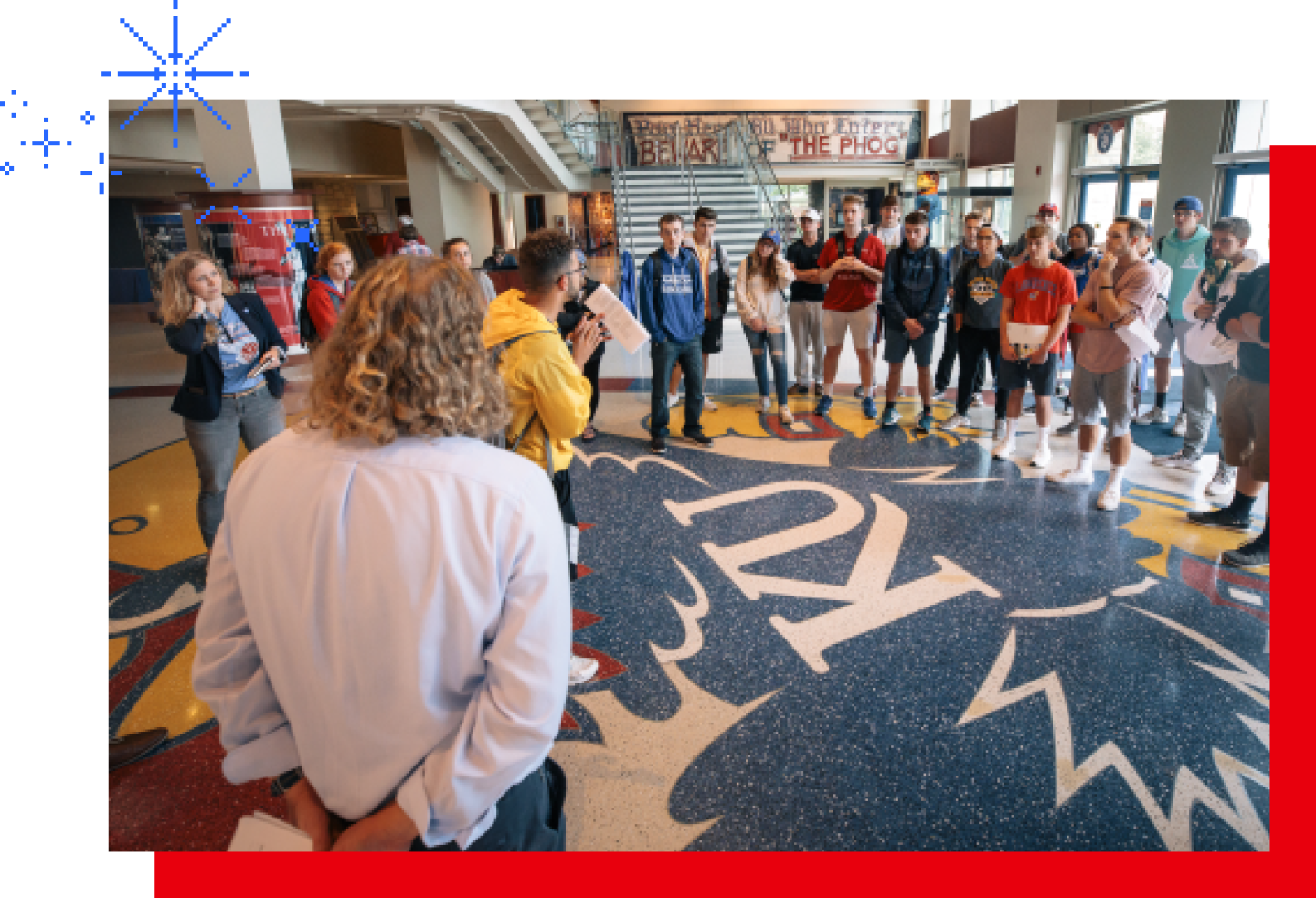 A group of new KU students gather in the common hall with the Jayhawk logo on the floor.
