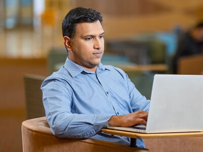 A male SCU MBA student sitting in common area while working on laptop.