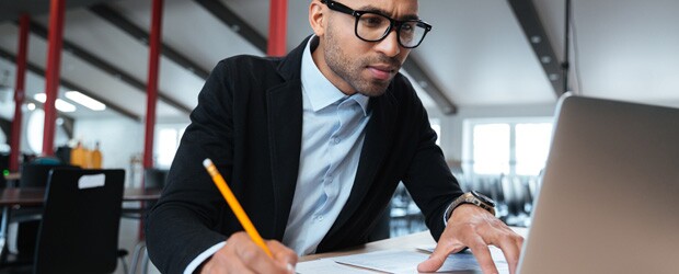 Man with pencil and paper looking at laptop.
