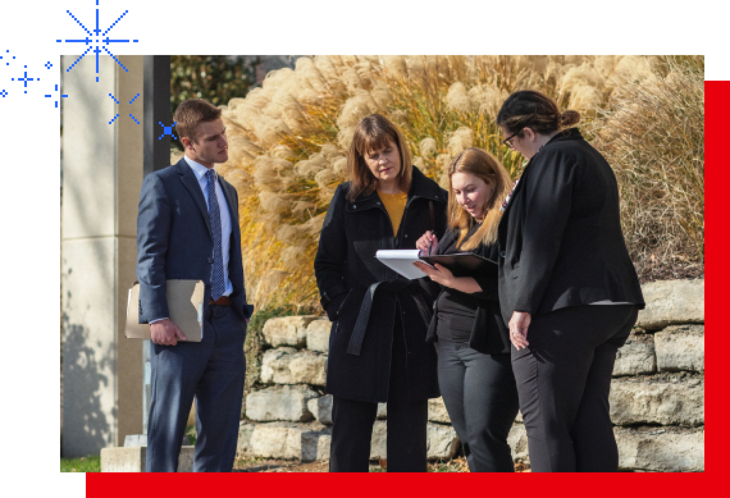 A group of male and female KU MSBA students review lesson notes while standing on campus grounds.