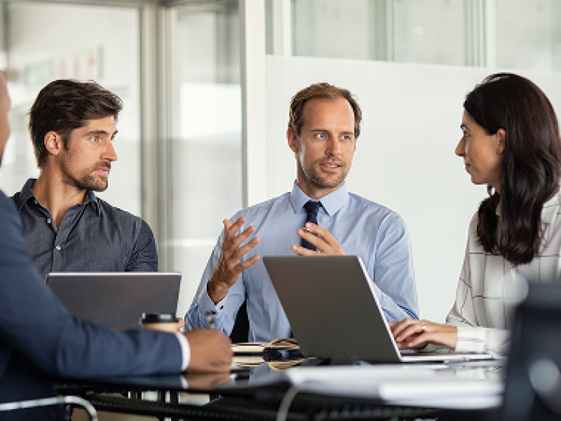 Group of business professionals sit around a table conducting a meeting.