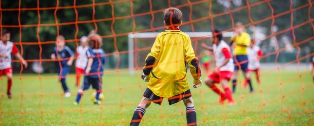 kids-playing-soccer-camera-behind-goalie-in-yellow-orange-net