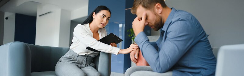 mental health professional holding a clipboard and working one-on-one with a male client