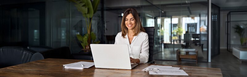 A woman using a laptop application for work at a table workspace in the office.