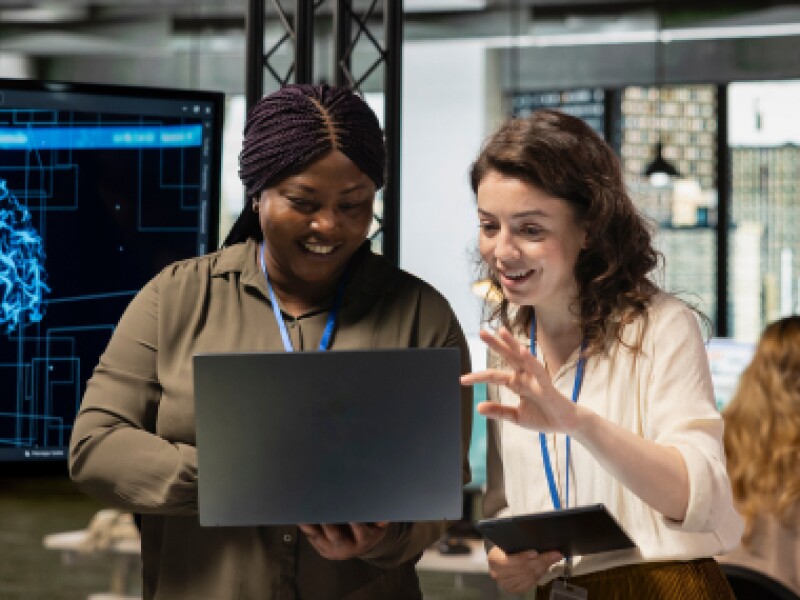 Two female analysts review metrics on laptop.
