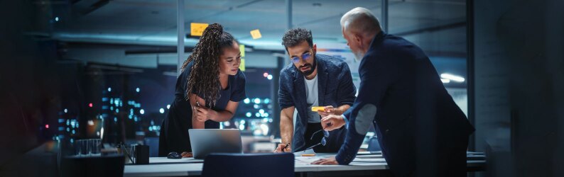 A diverse team of executives discuss financial investments during a night meeting.