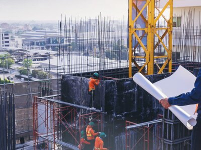 Civil engineer inspecting and working outdoors building side with blueprints.