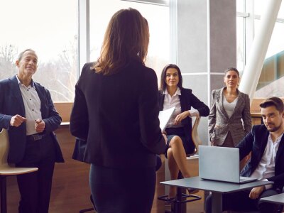 Various businessmen listen to female business leader during corporate meeting.
