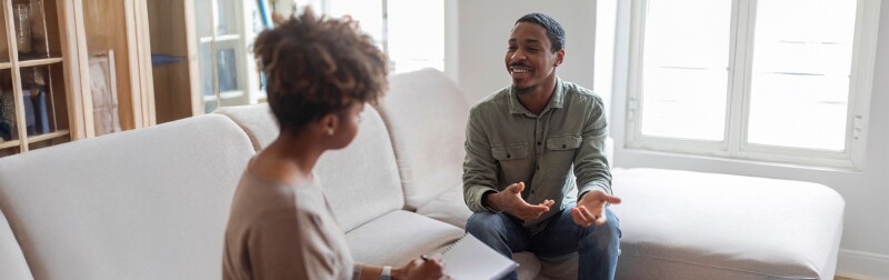 An African American counselor talking with a client in a bright, comfortable therapy room