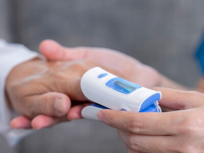 A nurse in uniform, with stethoscope, reads a patient's pulse oximeter