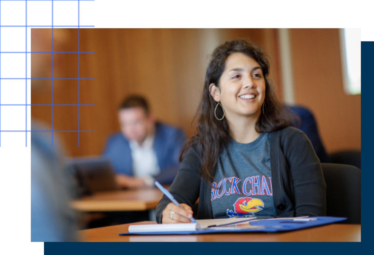 A female KU student is smiling while writing notes in a notebook.