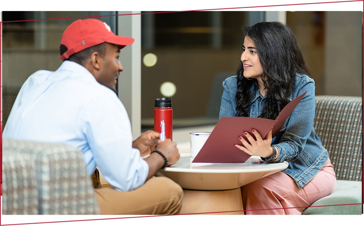 Two students seated together discussing the contents of a red folder