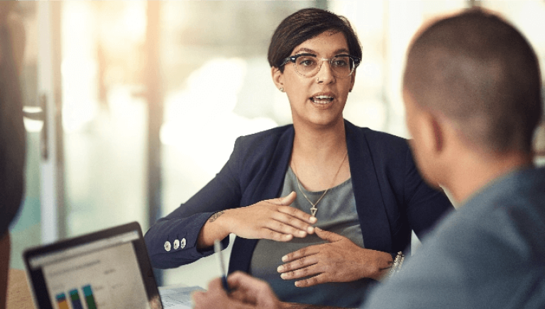 Woman in glasses and blazer in discussion with man using a laptop displaying charts