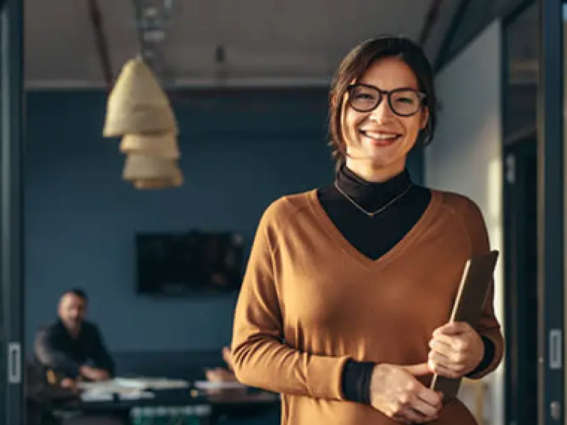 Professional female smiling while standing in a meeting room doorway.