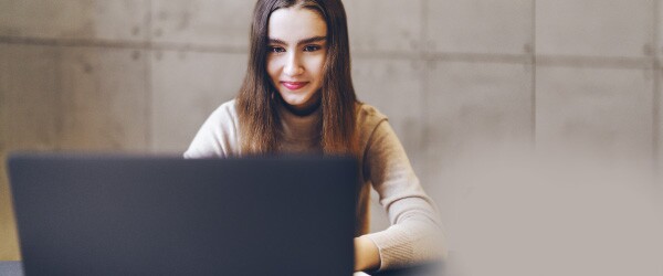 woman-in-tan-sitting-at-laptop-in-front-of-tan-stone-wall
