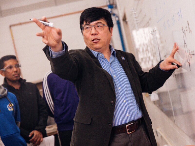 A male KU professor is standing in front of a whiteboard.