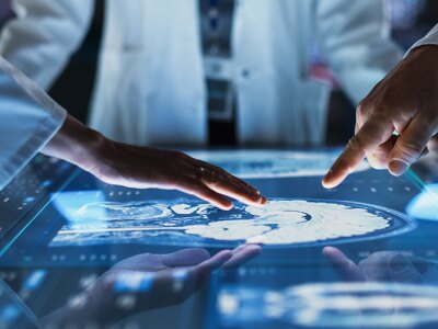 Doctors Interacting With Touch Screen On Table With MRI Scans Of Brain On Display.