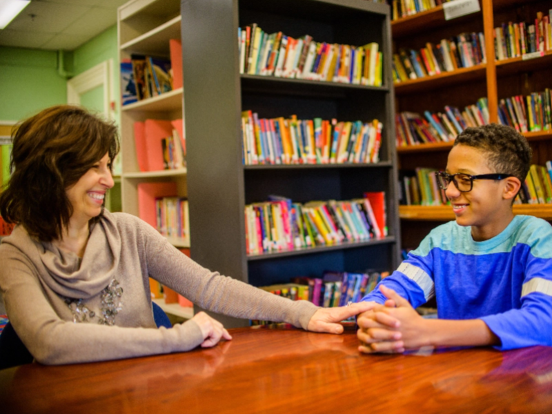 School counselor seated in library speaking with boy