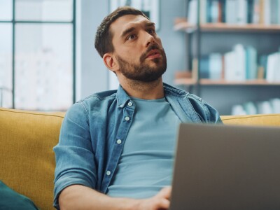 Man sitting on a sofa with a laptop, deep in thought, reflecting on possibilities