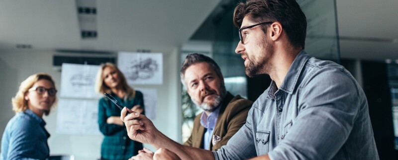 Man talks in meeting with three coworkers