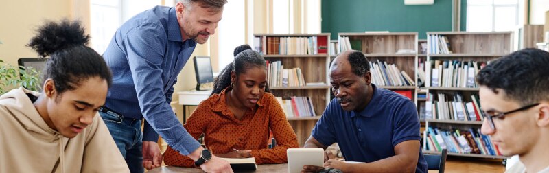 Caucasian English language teacher supporting immigrant students during lesson.