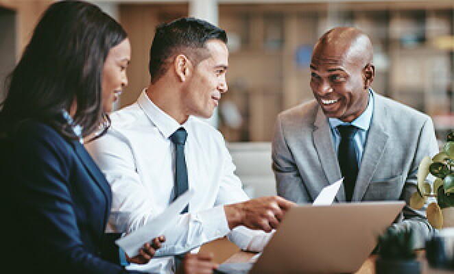 Three colleagues talking over a table with laptops