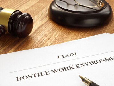 A document reading "Claim: Hostile Work Environment" is lying on a desk next to a gavel.