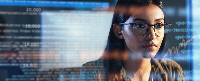A woman analyzing data on a screen, with reflections of digital information overlaid on her glasses