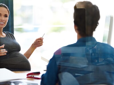 A pregnant woman is sitting at a table in a discussion with two coworkers.