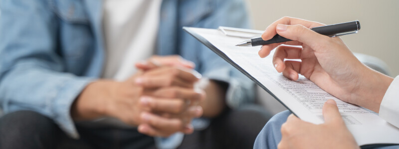 A close up of a mental health counselor taking notes during a session with a patient facing them
