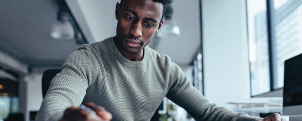 Man by a computer looking down at his notes