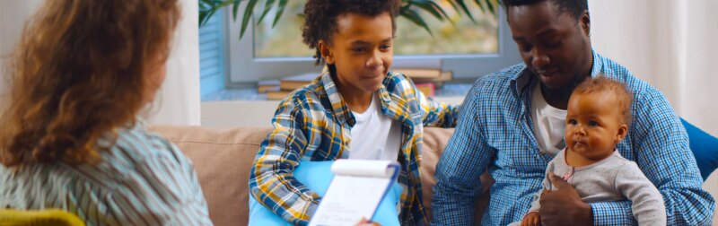 Social worker consulting smiling young single father with kids at home.