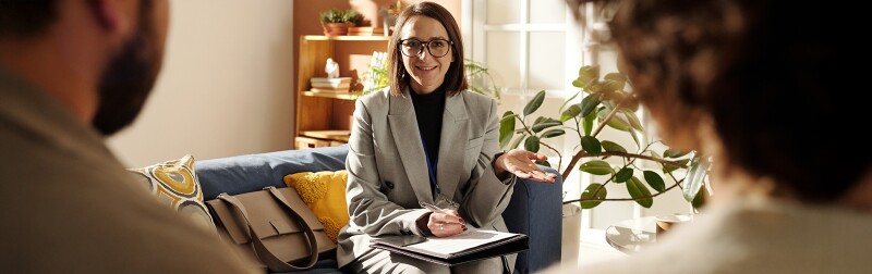 Social worker in suit sitting on sofa in the living room and talking to foster parents about custody at meeting at home