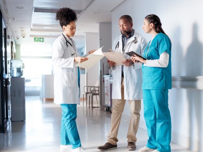 Three healthcare professionals standing in the hallway of a hospital going over charts