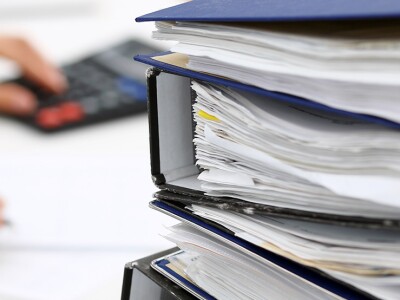 Binders with papers are waiting in the foreground, woman conducting an audit in the background