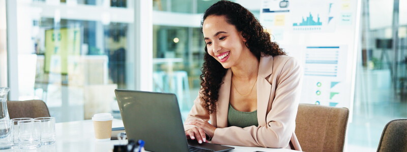 A businesswoman smiles as she sits at her laptop, working in her accounting job.
