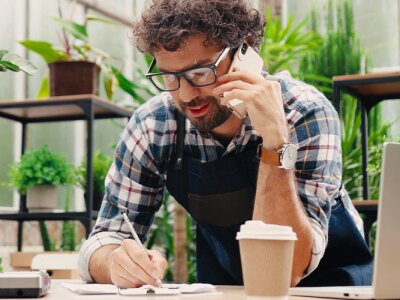 Businessman in a small floral shop on a cellphone taking order details