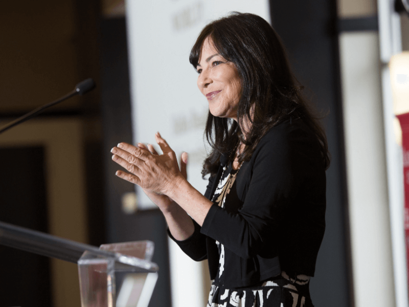 Woman clapping at podium while delivering speech at Bradley University