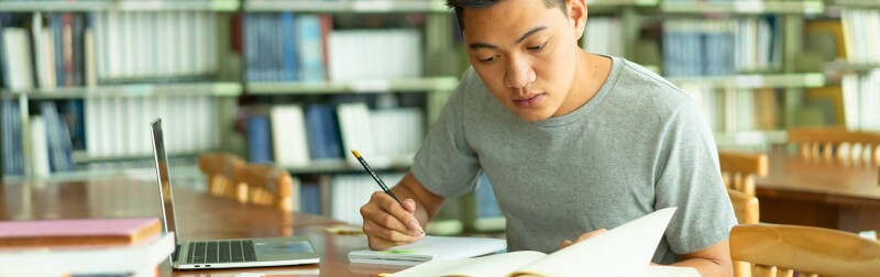 Male student studying and reading book in library